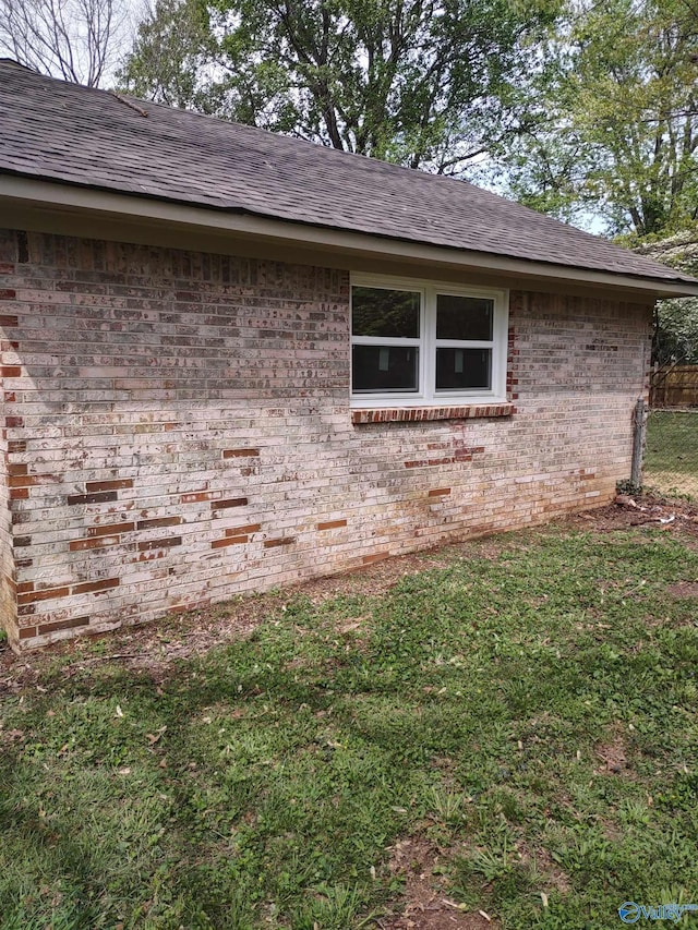 view of property exterior featuring brick siding, a shingled roof, and a lawn