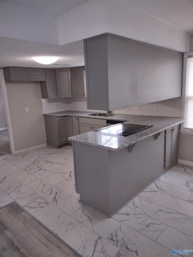 kitchen featuring light stone countertops, a peninsula, a textured ceiling, marble finish floor, and a sink
