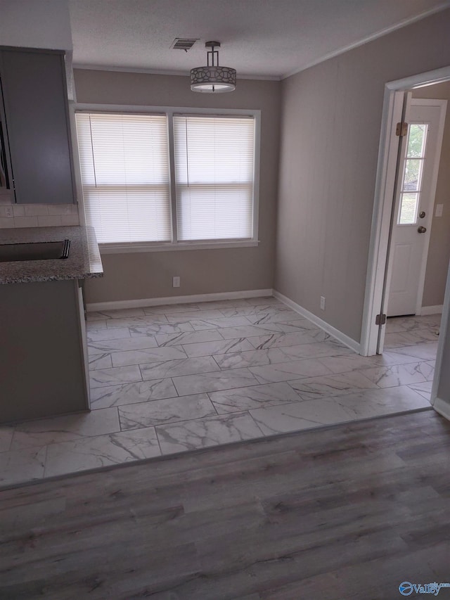 unfurnished dining area featuring baseboards, a textured ceiling, crown molding, visible vents, and marble finish floor