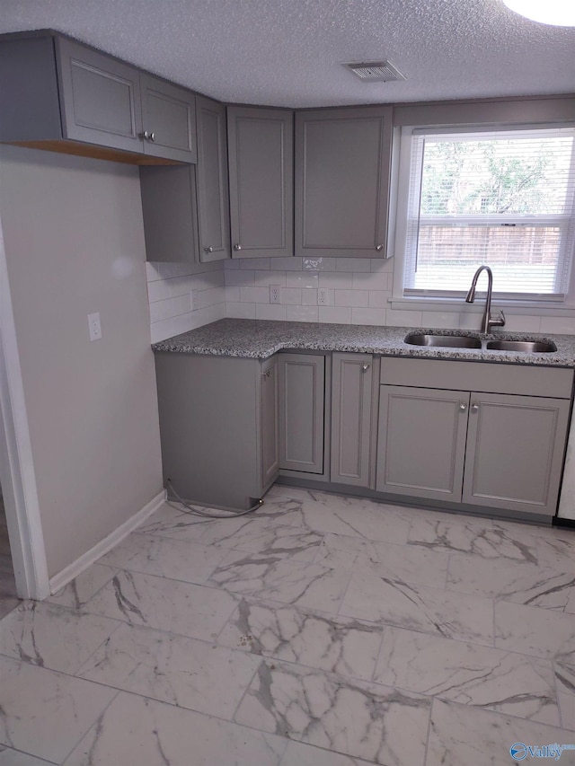 kitchen with visible vents, a sink, gray cabinets, backsplash, and marble finish floor