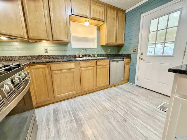 kitchen with appliances with stainless steel finishes, wooden walls, sink, dark stone countertops, and light hardwood / wood-style floors