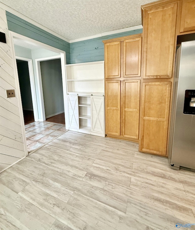 kitchen with wood walls, light wood-type flooring, ornamental molding, stainless steel fridge with ice dispenser, and a textured ceiling