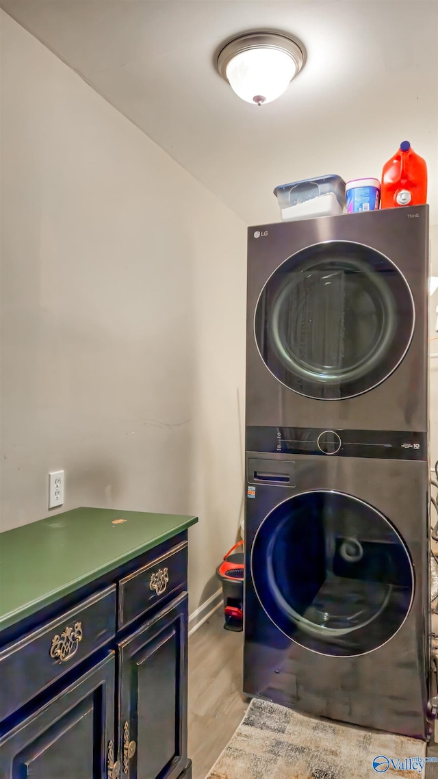 clothes washing area featuring light hardwood / wood-style flooring, cabinets, and stacked washer and clothes dryer