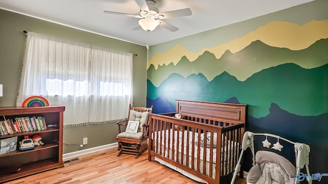 bedroom with ceiling fan, hardwood / wood-style floors, and a nursery area