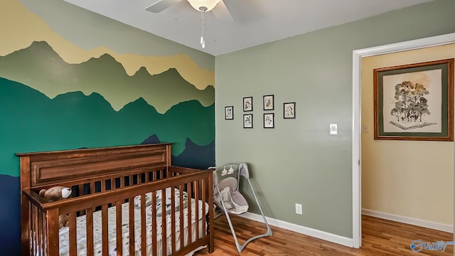 bedroom with a crib, hardwood / wood-style floors, and ceiling fan