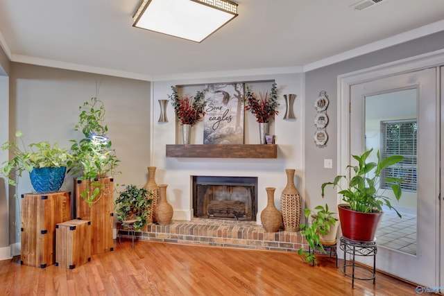 sitting room with wood-type flooring, a brick fireplace, and crown molding