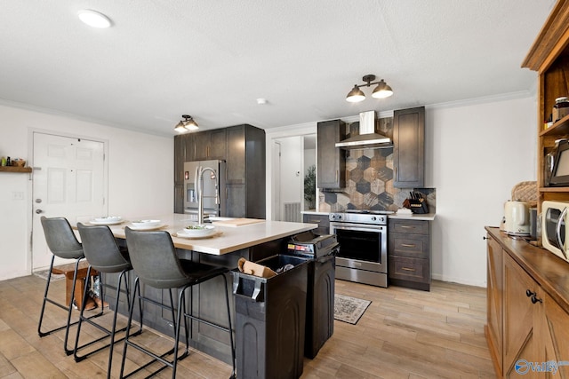 kitchen featuring tasteful backsplash, a kitchen bar, appliances with stainless steel finishes, light wood-type flooring, and wall chimney range hood