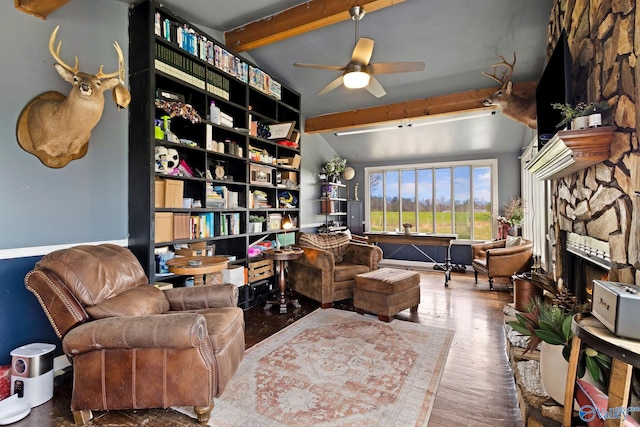 living room featuring a stone fireplace, vaulted ceiling with beams, ceiling fan, and hardwood / wood-style floors