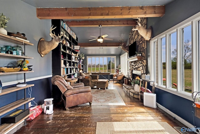 living area featuring baseboards, beamed ceiling, wood finished floors, and a ceiling fan