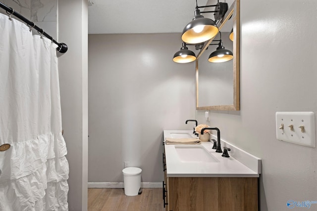 full bathroom with a shower with shower curtain, baseboards, double vanity, wood finished floors, and a sink