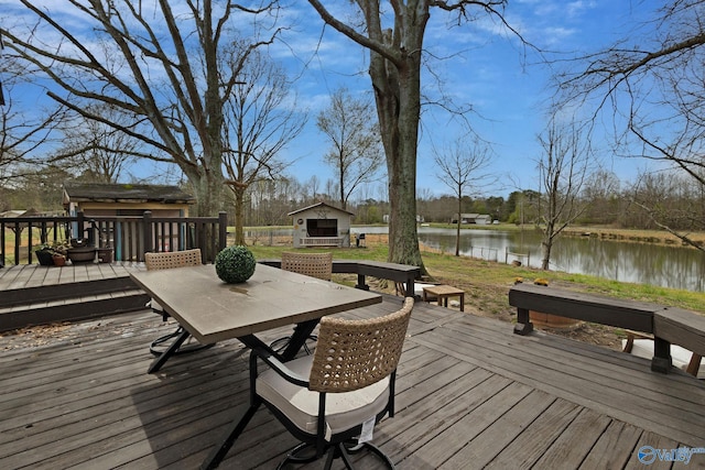 wooden terrace with an outdoor structure, outdoor dining area, a water view, and a storage shed