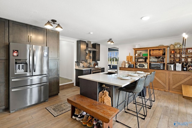 kitchen featuring light countertops, light wood-style flooring, wall chimney exhaust hood, stainless steel appliances, and a sink