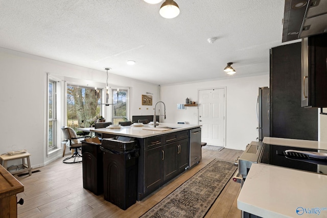 kitchen featuring light countertops, a sink, a center island with sink, stainless steel appliances, and light wood-style floors