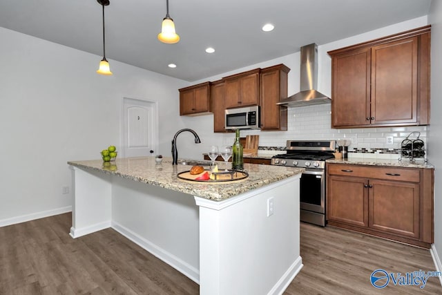 kitchen featuring wall chimney range hood, sink, hanging light fixtures, dark hardwood / wood-style floors, and stainless steel appliances