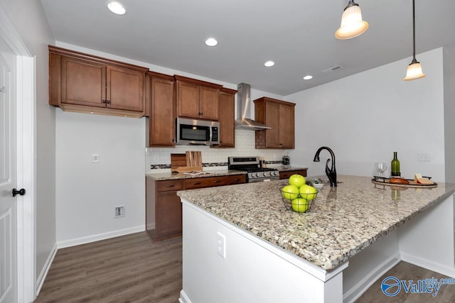 kitchen with dark wood-type flooring, wall chimney range hood, hanging light fixtures, kitchen peninsula, and stainless steel appliances