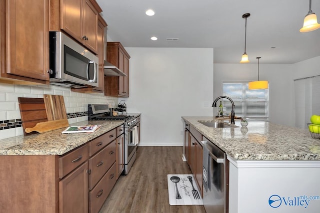 kitchen with stainless steel appliances, sink, decorative light fixtures, hardwood / wood-style floors, and an island with sink