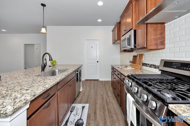 kitchen featuring appliances with stainless steel finishes, light stone counters, wall chimney range hood, sink, and light hardwood / wood-style floors