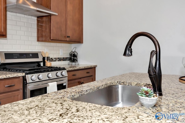 kitchen featuring decorative backsplash, light stone counters, exhaust hood, and gas range