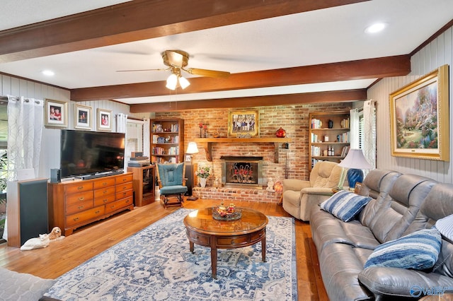 living room featuring wood-type flooring, a fireplace, ceiling fan, built in features, and beam ceiling