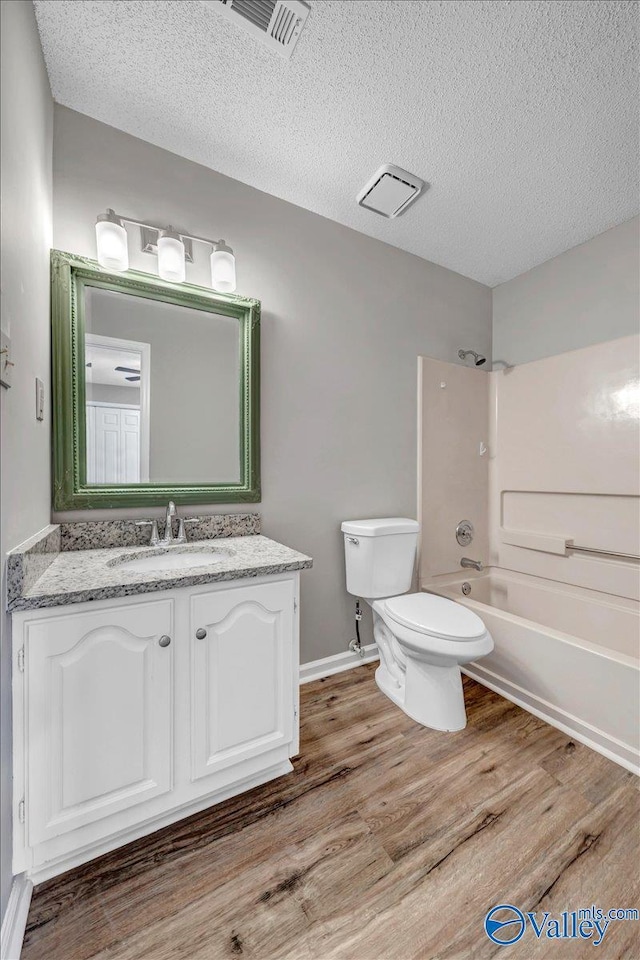 full bathroom with tub / shower combination, vanity, a textured ceiling, hardwood / wood-style floors, and toilet