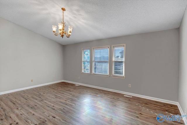 spare room featuring hardwood / wood-style floors, a textured ceiling, and an inviting chandelier