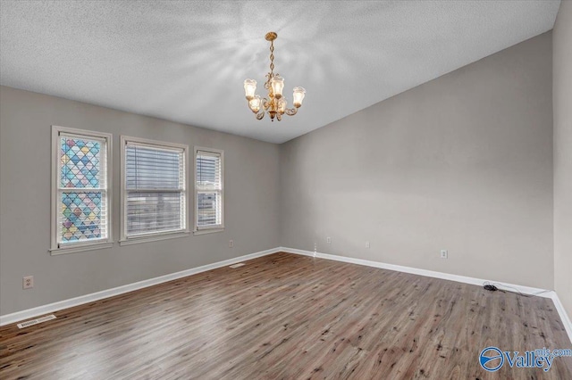 empty room featuring wood-type flooring, a textured ceiling, and a notable chandelier