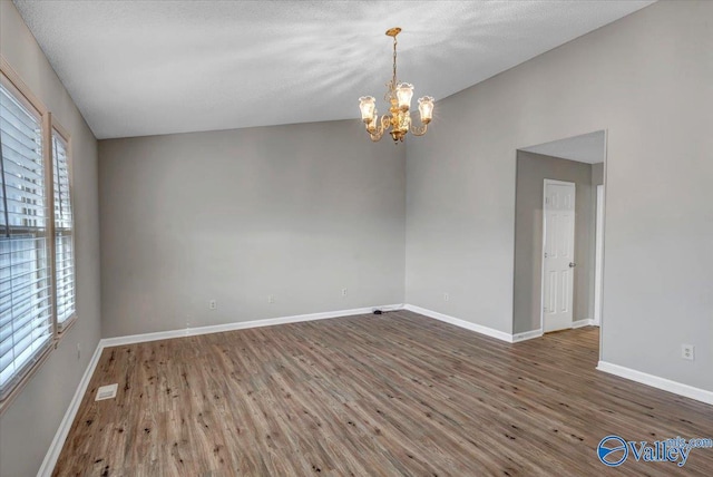 spare room featuring a textured ceiling, a healthy amount of sunlight, dark wood-type flooring, and a chandelier