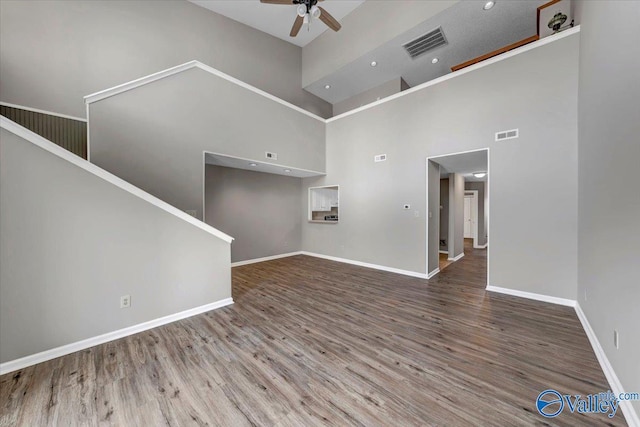 unfurnished living room featuring ceiling fan, wood-type flooring, and a towering ceiling