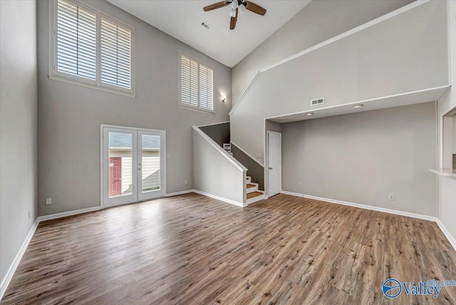 unfurnished living room featuring hardwood / wood-style floors, ceiling fan, high vaulted ceiling, and french doors