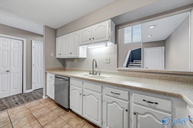 kitchen featuring sink, stainless steel dishwasher, light hardwood / wood-style floors, a textured ceiling, and white cabinets