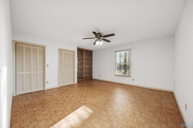 unfurnished bedroom with parquet flooring, ceiling fan, and multiple closets