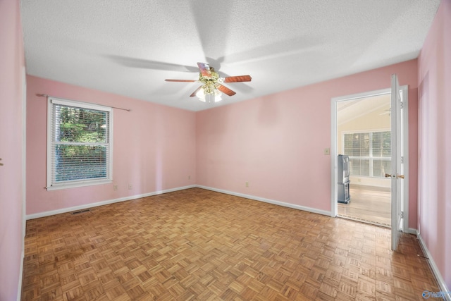 empty room with ceiling fan, a textured ceiling, plenty of natural light, and light parquet flooring