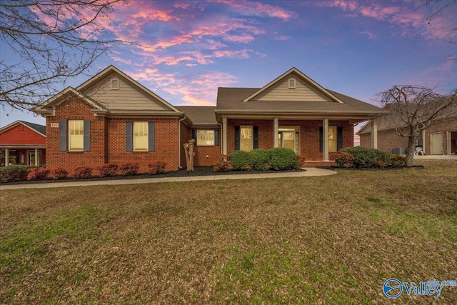 view of front of property featuring covered porch, a lawn, and brick siding