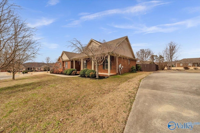 view of front of house featuring concrete driveway, brick siding, fence, and a front lawn