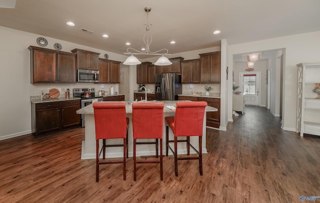 kitchen with decorative backsplash, a kitchen bar, appliances with stainless steel finishes, an island with sink, and dark hardwood / wood-style flooring