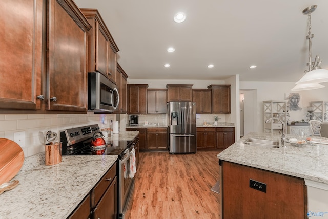 kitchen with light wood-type flooring, appliances with stainless steel finishes, sink, and backsplash