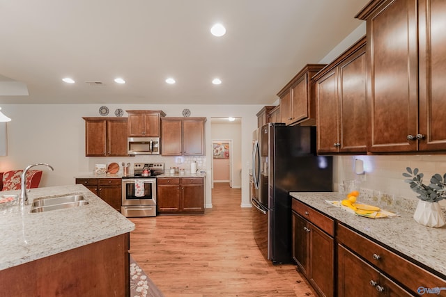 kitchen with light stone counters, appliances with stainless steel finishes, light hardwood / wood-style floors, and backsplash