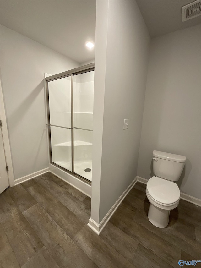 bathroom with wood-type flooring, toilet, and a shower with door