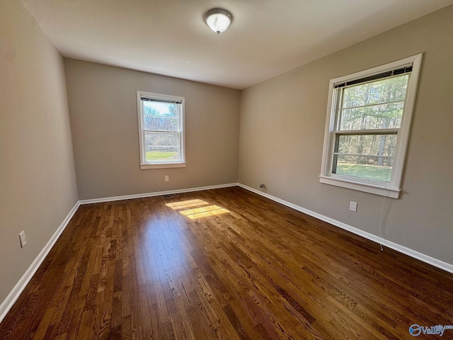 spare room with dark wood-style floors, visible vents, and baseboards