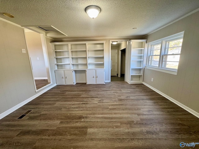 unfurnished bedroom featuring a textured ceiling, visible vents, built in study area, dark wood-style floors, and crown molding