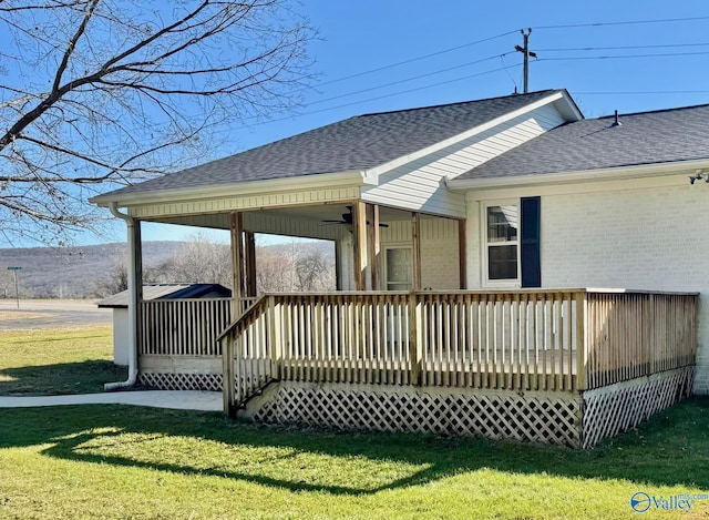 back of house featuring roof with shingles, a yard, a deck, and brick siding