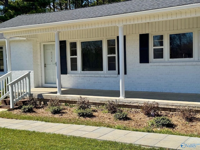 doorway to property with covered porch, roof with shingles, and brick siding