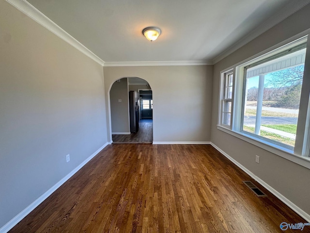 unfurnished room featuring a healthy amount of sunlight, visible vents, arched walkways, and dark wood finished floors