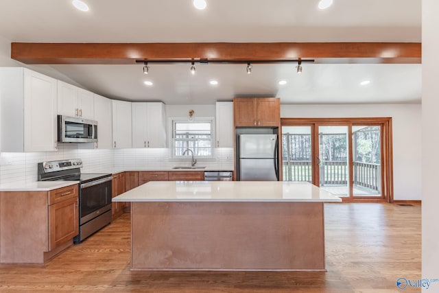 kitchen featuring light countertops, decorative backsplash, light wood-style flooring, appliances with stainless steel finishes, and a sink