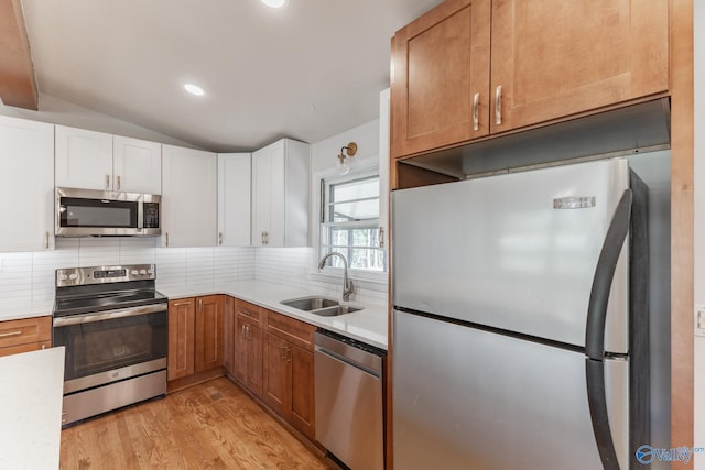 kitchen with a sink, tasteful backsplash, stainless steel appliances, light wood finished floors, and lofted ceiling