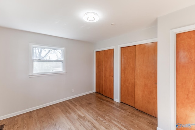 unfurnished bedroom featuring visible vents, baseboards, light wood-style floors, and multiple closets