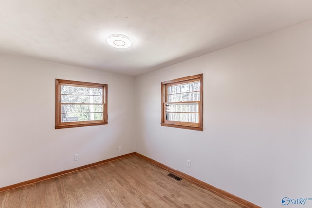 empty room with light wood-style flooring, a healthy amount of sunlight, visible vents, and baseboards