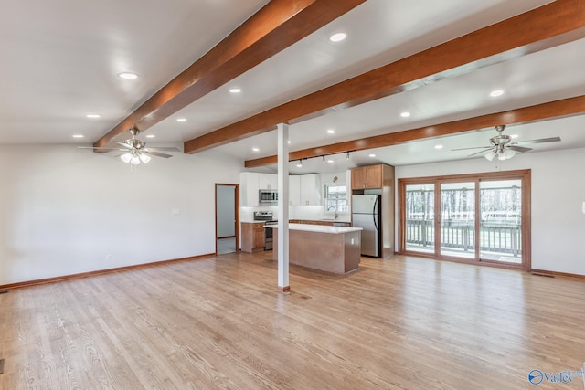 unfurnished living room with a ceiling fan, baseboards, a sink, beamed ceiling, and light wood-type flooring