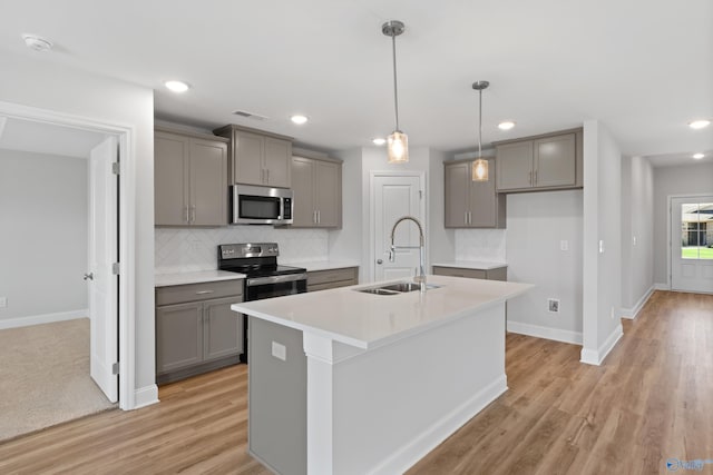 kitchen with sink, gray cabinets, stainless steel appliances, and an island with sink