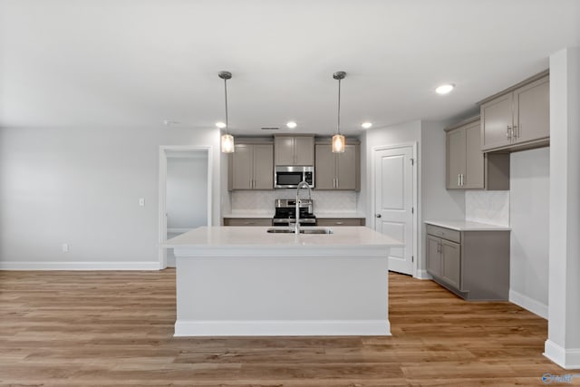 kitchen with gray cabinets, appliances with stainless steel finishes, and a kitchen island with sink